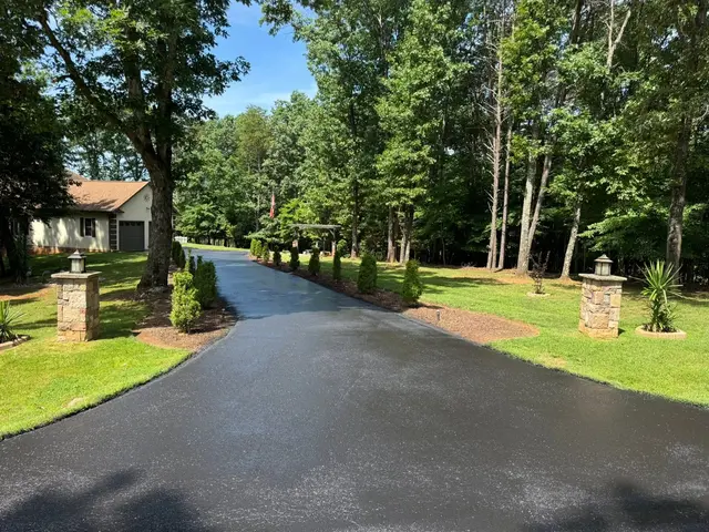 Freshly paved tree-lined driveway entrance with stone pillars